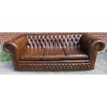 A vintage three seater Chesterfield sofa upholstered in distressed chestnut brown leather, raised on