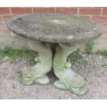 A small circular reconstituted stone garden table with carved top, raised on three moulded fish/