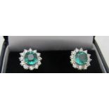 A fine pair of 18ct white gold cushion cut emerald and round brilliant cut diamond halo earrings.