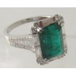An 18ct white gold emerald and diamond cluster ring with diamond shoulders, emerald cut emerald 3.
