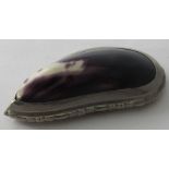 A white metal mounted mussel shell made into a snuff box. The back embossed with foliate design.