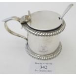 A silver drum shaped mustard pot with gadroon border decoration and thumb piece, blue liner,