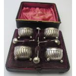 A set of four circular silver salts with spiral fluted decoration and matching salt spoons, London