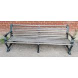 A large cast iron park bench with teak slatted seat and heavy end supports depicting lions heads,