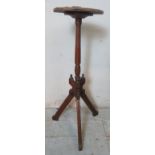 An Arts & Crafts mahogany and oak torchere with turned column and carved tripod base with finials.