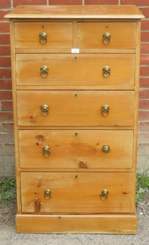 A tall pine chest of two over three long drawers with brass drop ring handles, raised on a plinth