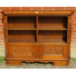 A vintage carved oak low open bookcase comprising four shelves over a cupboard base flanked by a