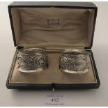 A pair of silver napkin rings with embossed flowers & scroll decoration, Birmingham 1897 and 1902,