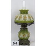 An ornately decorated converted oil lamp with green shade and reservoir supported by gilt metal