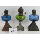 Three antique metal based oil lamps, two with blue glass reservoirs and one with green. Tallest