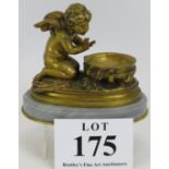 An antique gilt bronze figure of a winged cherub crouching over a cauldron raised on a grey marble