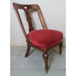 A Victorian oak low bedroom occasional chair with roundel carved back splat raised on tapering