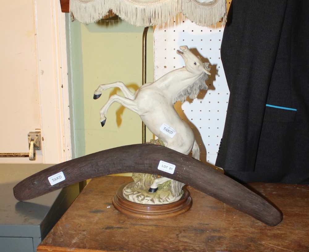 A HAND CARVED BOOMERANG together with a decorative table light in the form of a prancing white horse