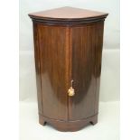 A GEORGIAN DESIGN MAHOGANY FLOOR STANDING BOW FRONT CORNER CUPBOARD, fitted two doors raised on