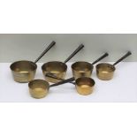 A GRADUATED COLLECTION OF SIX 19TH CENTURY BRASS SAUCEPANS with tapering tubular iron handles, the