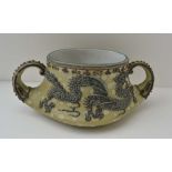 AN EARLY 20TH CENTURY JAPANESE CERAMIC TWO-HANDLED POT, bearing raised dragon decoration, on a green