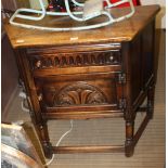 A REPRODUCTION OAK FINISHED SIDE CABINET of canted form, having carved single drawer over carved