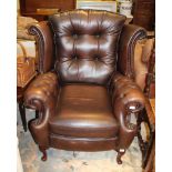 A CHOCOLATE BROWN LEATHER EFFECT UPHOLSTERED WING BACK ARMCHAIR with decorative stud work
