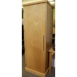 A FREESTANDING BLONDE WOOD WARDROBE with a single door opening to reveal full width hanging rail,