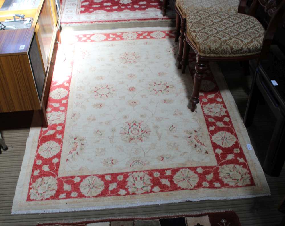 A WOVEN WOOLED PAKISTANI FLOOR RUG with pale central field & red floral design guard border, 178cm x