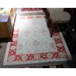 A WOVEN WOOLED PAKISTANI FLOOR RUG with pale central field & red floral design guard border, 178cm x