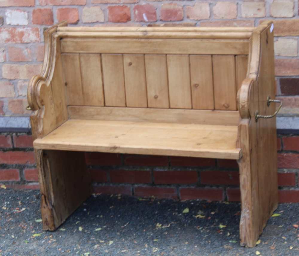 A 19TH CENTURY PINE FORMED TWO-SEATER PEW / SETTLE, having prayer book shelved back, on shaped plank