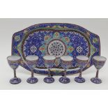 A 20TH CENTURY PERSIAN ENAMEL TRAY with six small drinking cups on stems, stylised floral decoration