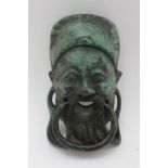 A CAST BRONZE DOOR KNOCKER in the form of the mask of a happy Chinese scholar, green verdigris
