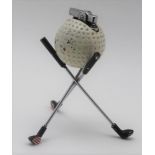 A GOLF BALL TABLE LIGHTER, the ball raised on a cross stand of the golf clubs, 13cm high