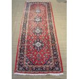 A WOVEN WOOLLEN FLOOR PERSIAN DESIGN LONG RUG being red ground central field, housed within triple