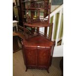 AN ORIENTAL CORNER UNIT with three open fronted shelves, fretwork sides, base with two cupboard door