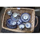 A TWIN HANDLED WOVEN WICKER BASKET CONTAINING A SELECTION OF BOOTHS OLD WILLOW TEA WARES