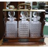 A BRASS & OAK TANTALUS containing three hobnail cut decanters & stoppers