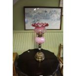 AN EARLY 20TH CENTURY BRASS BASED OIL LAMP with pink glass reservoir, and tinted crimple edged shade