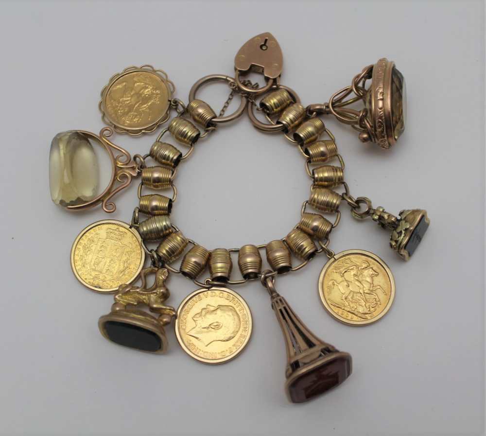 A YELLOW METAL CHARM BRACELET set with four framed full sovereigns, and five fob seals, some