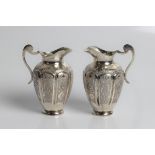 A pair of unmarked white metal jugs with decorative design on eight panelled body, 11cm x 7.5cm x