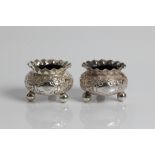 A pair of Victorian silver salts with blue glass liners on three ball feet, decorated with floral