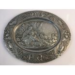 A pewter decorative tray with women and sheep scene to centre surrounded by fruit and birds to