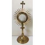 A brass monstrance with central glass case surrounded by sun burst design and cross to top, approx