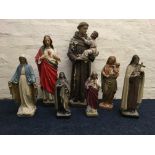 Seven painted plaster and resin figurines depicting religious figures including Saint Anthony with