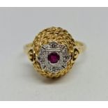 A hallmarked 18ct yellow gold ruby and diamond ring, set with a central round cut ruby surrounded by