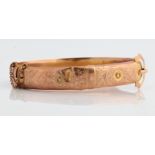 A hallmarked 9ct yellow gold engraved hinged buckle design bangle with safety chain, approx.