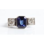 A sapphire and diamond three stone ring, the central emerald-cut sapphire (possibly synthetic)