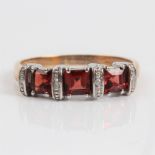 A three stone garnet ring with diamond accents, stamped 375, ring size R. IMPORTANT: Online