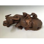 A large carved water buffalo, with glass eyes, with two children on top, length 36cm. IMPORTANT: