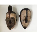 Two West African tribal carved face masks, with white face fronts, one topped with bird head.