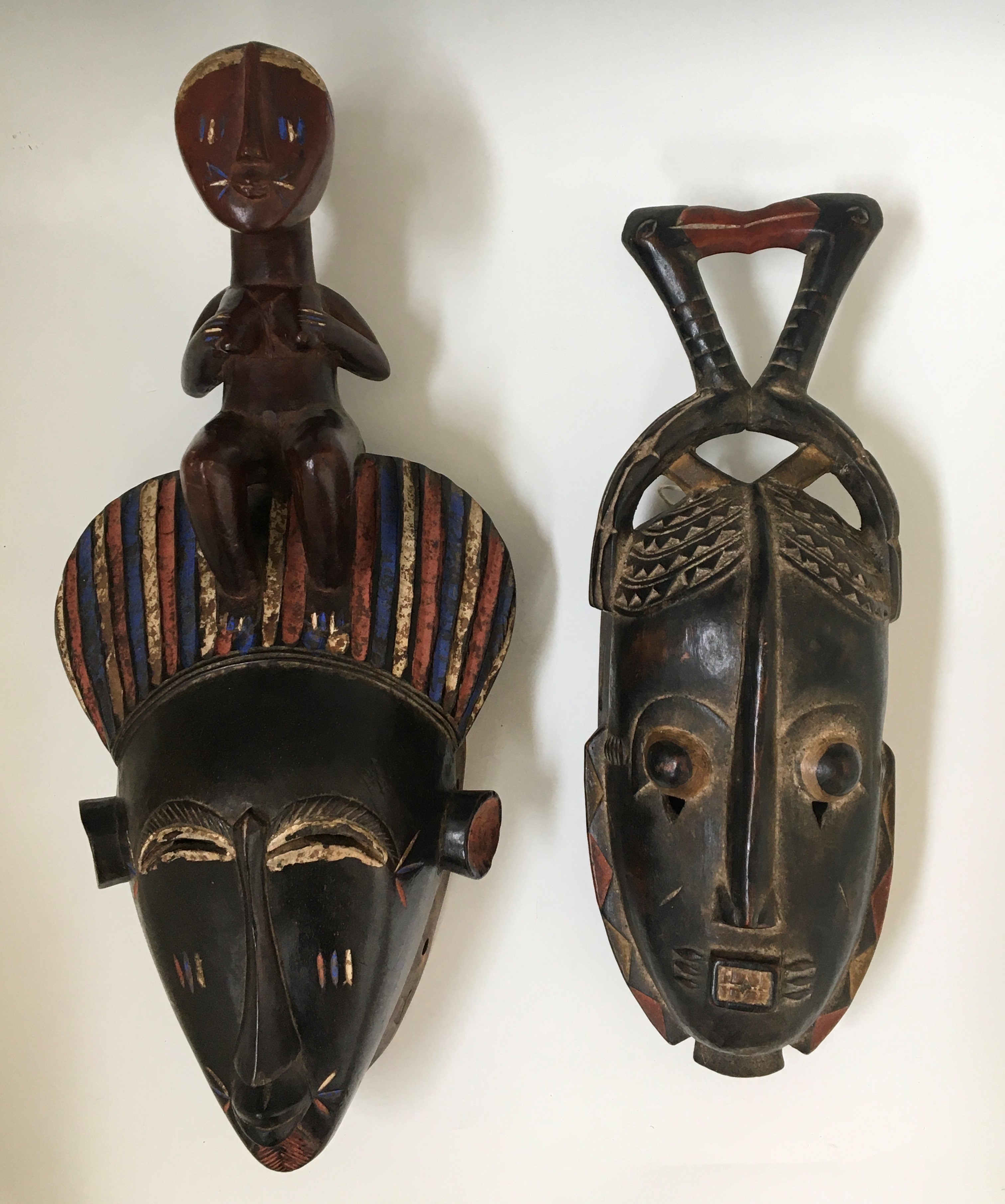 Two West African tribal face masks, one blue and red painted details topped with female, one