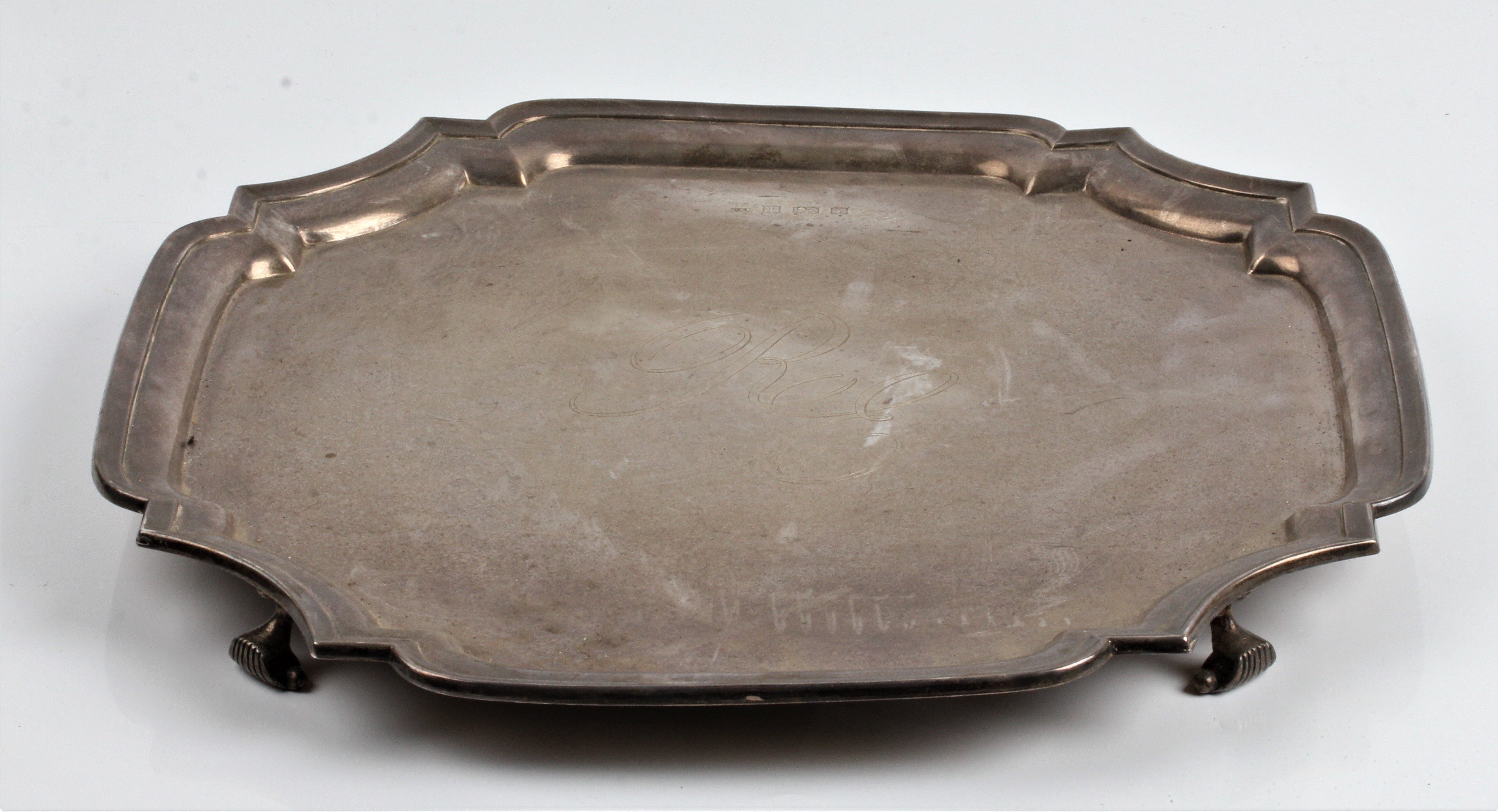 A silver salver with scalloped edging, engraved initials to centre, on four scroll feet, hallmarked