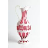 A bohemian cameo cranberry glass jug with grapevine detail to body, approx. height 33cm.