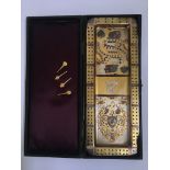 A cribbage board and four pins, silver and gold finished with playing cards motif, in leather